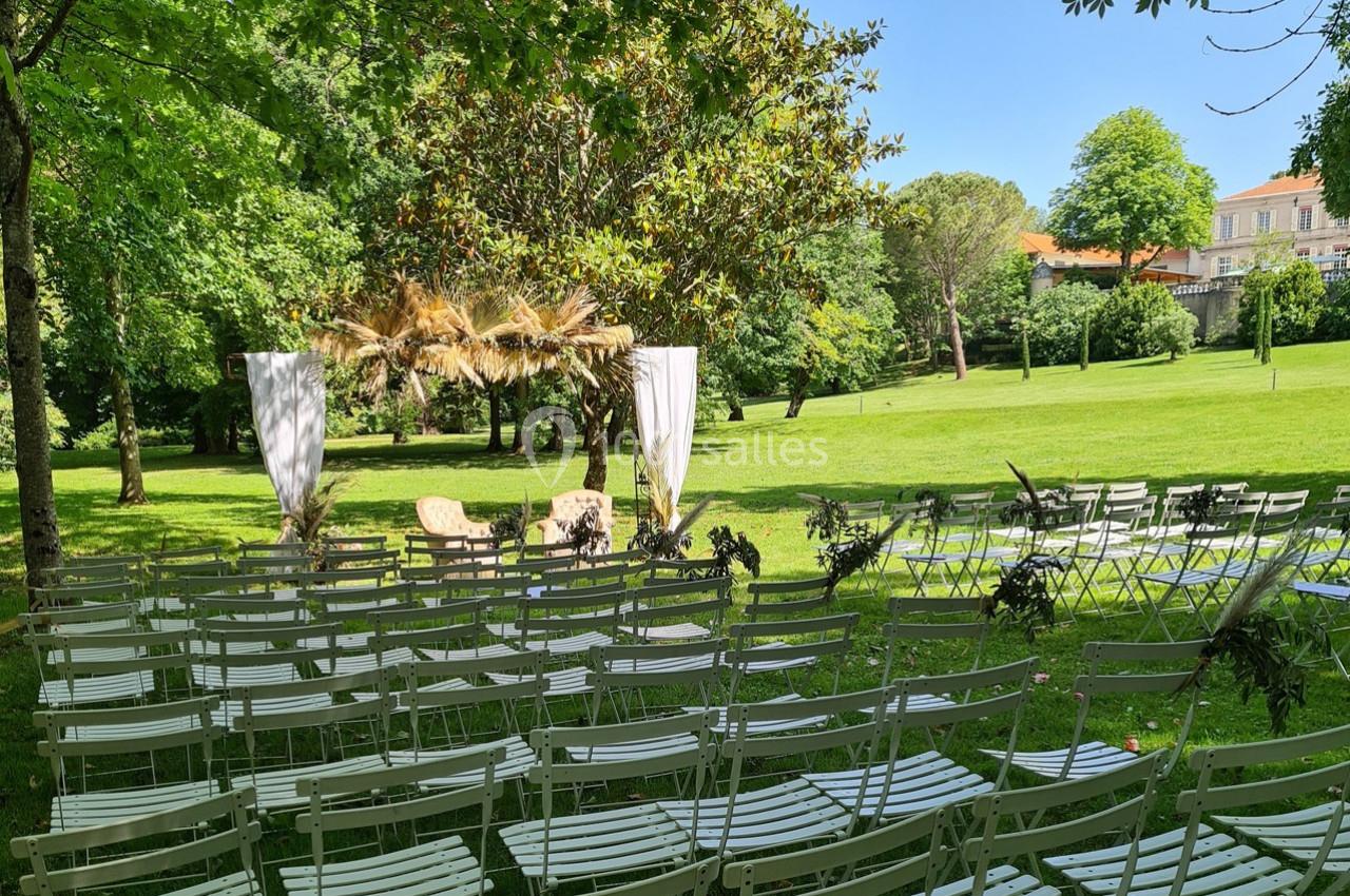 Chaises alignées en plein air face à une arche décorée de feuillages et de voilages dans un parc verdoyant.