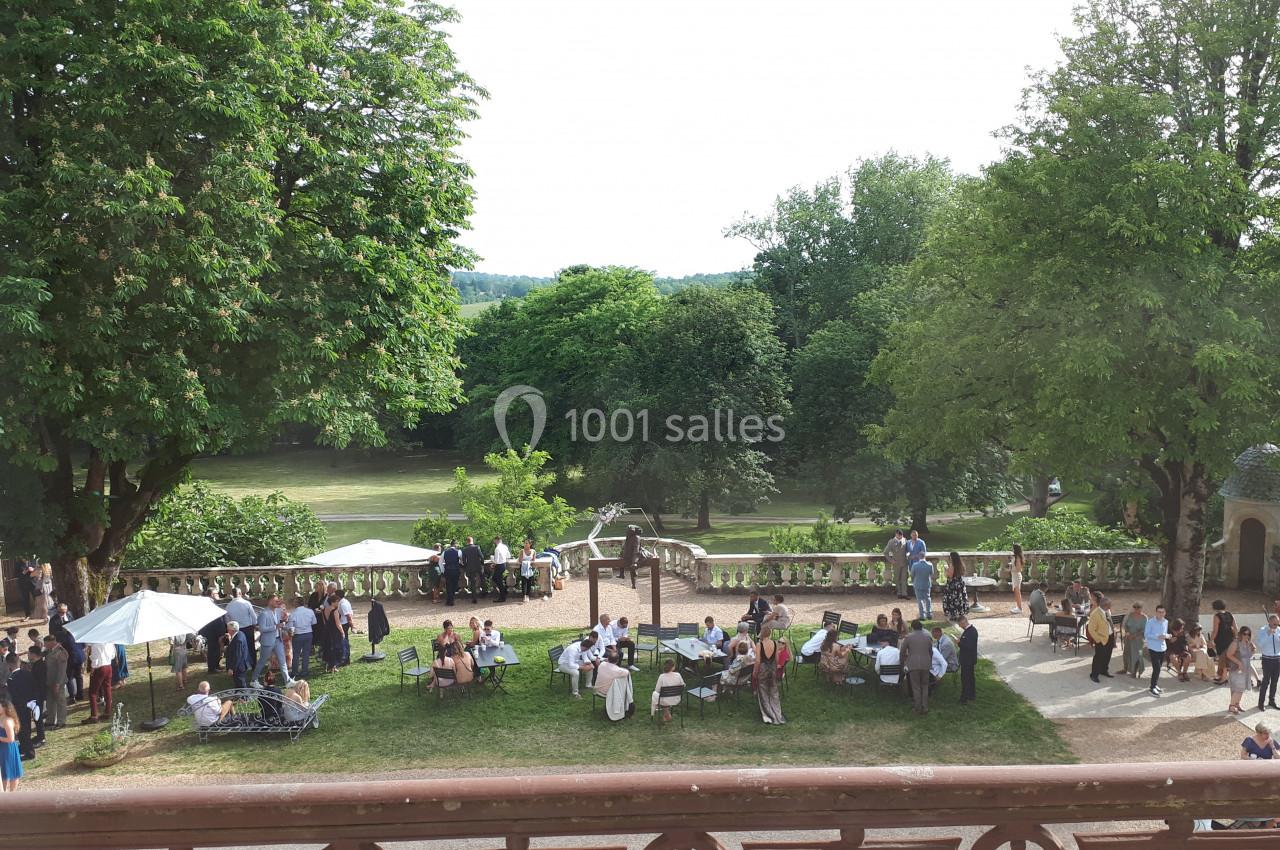 Groupe de personnes rassemblées dans un jardin arboré avec des parasols et une vue sur un parc verdoyant.
