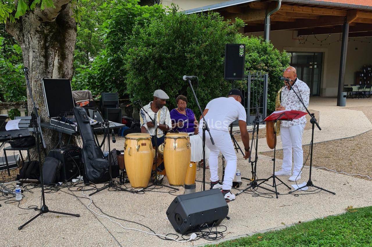 Un groupe de musiciens joue en extérieur avec des percussions, un saxophone et du matériel audio installé.