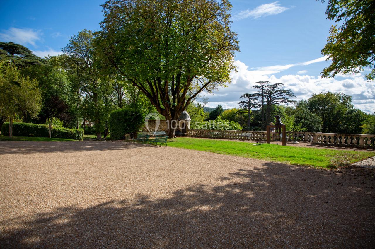 Allée gravillonnée bordée d'arbres et d'une pelouse, avec bancs et balustrade en pierre sous un ciel dégagé.