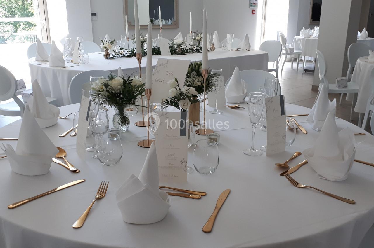 Table de réception élégamment dressée avec nappes blanches, couverts dorés, serviettes pliées et décorations florales.