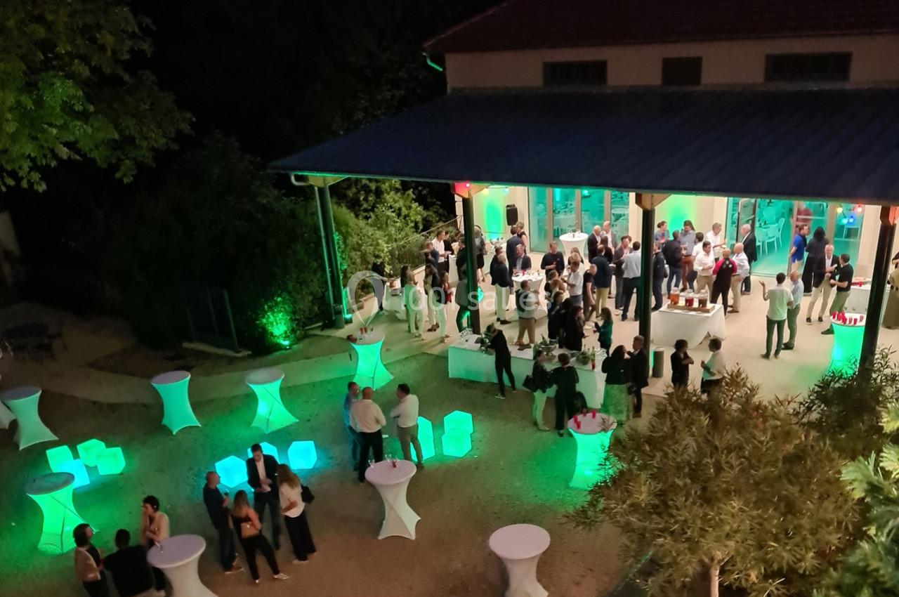 Vue nocturne d'une réception en plein air avec des invités rassemblés autour de tables éclairées de lumières colorées.
