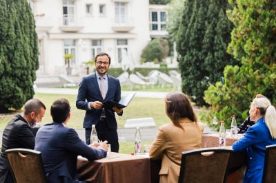 Une personne déguste une tartine garnie d'avocat et saumon, entourée de viennoiseries, fruits et boissons sur une table.