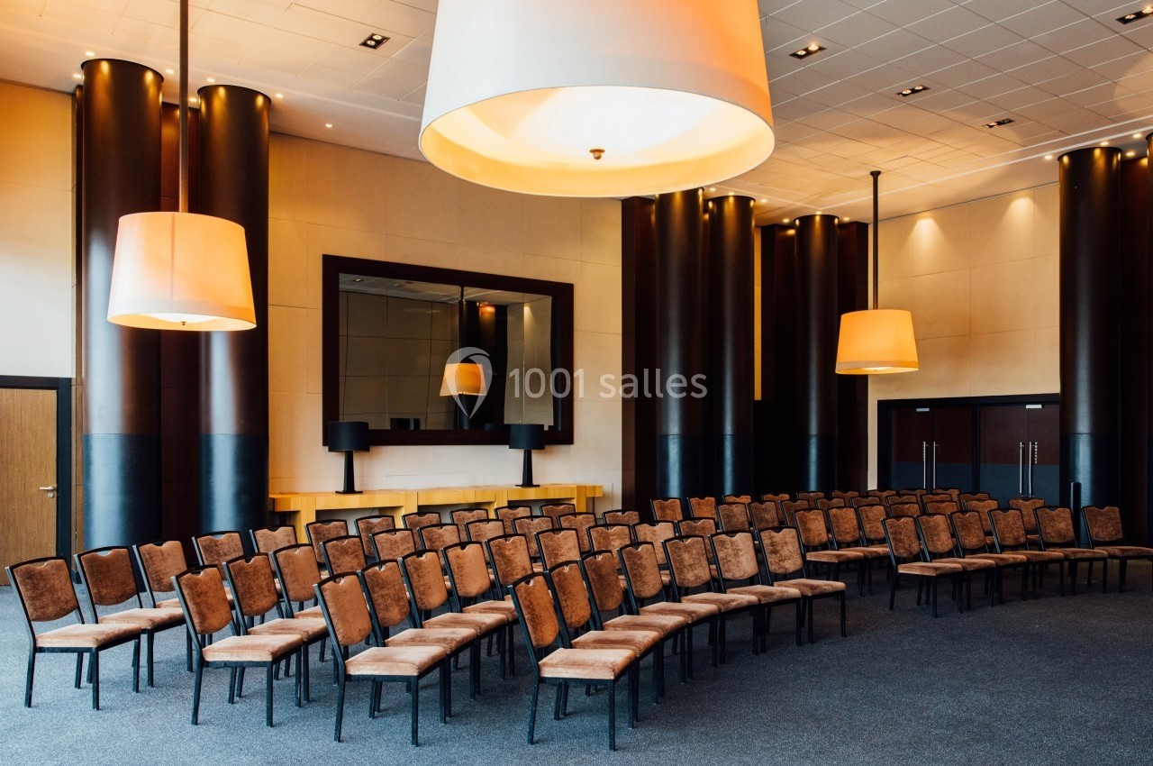 Salle de conférence avec des rangées de chaises vides, éclairée par des suspensions lumineuses modernes.