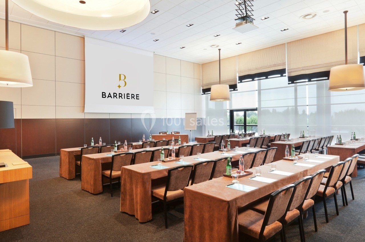 Salle de conférence lumineuse avec des tables alignées, chaises, écran de projection et matériel de réunion.