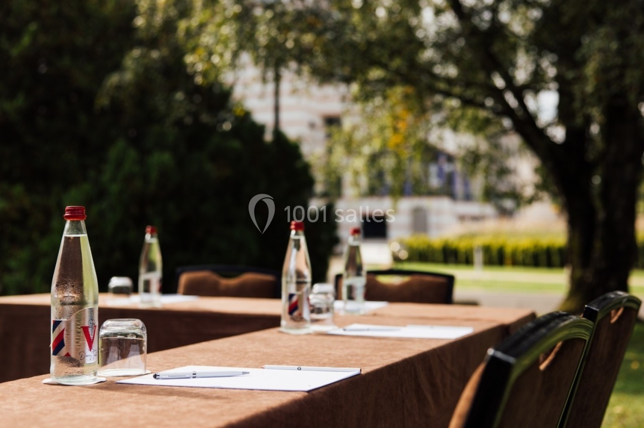 Tables en extérieur avec nappes marron, bouteilles d'eau, verres et documents, disposées pour une réunion ou un événement.
