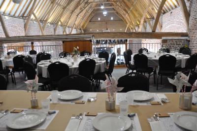 Salle de réception en briques avec tables rondes dressées, nappes blanches et décoration de mariage.