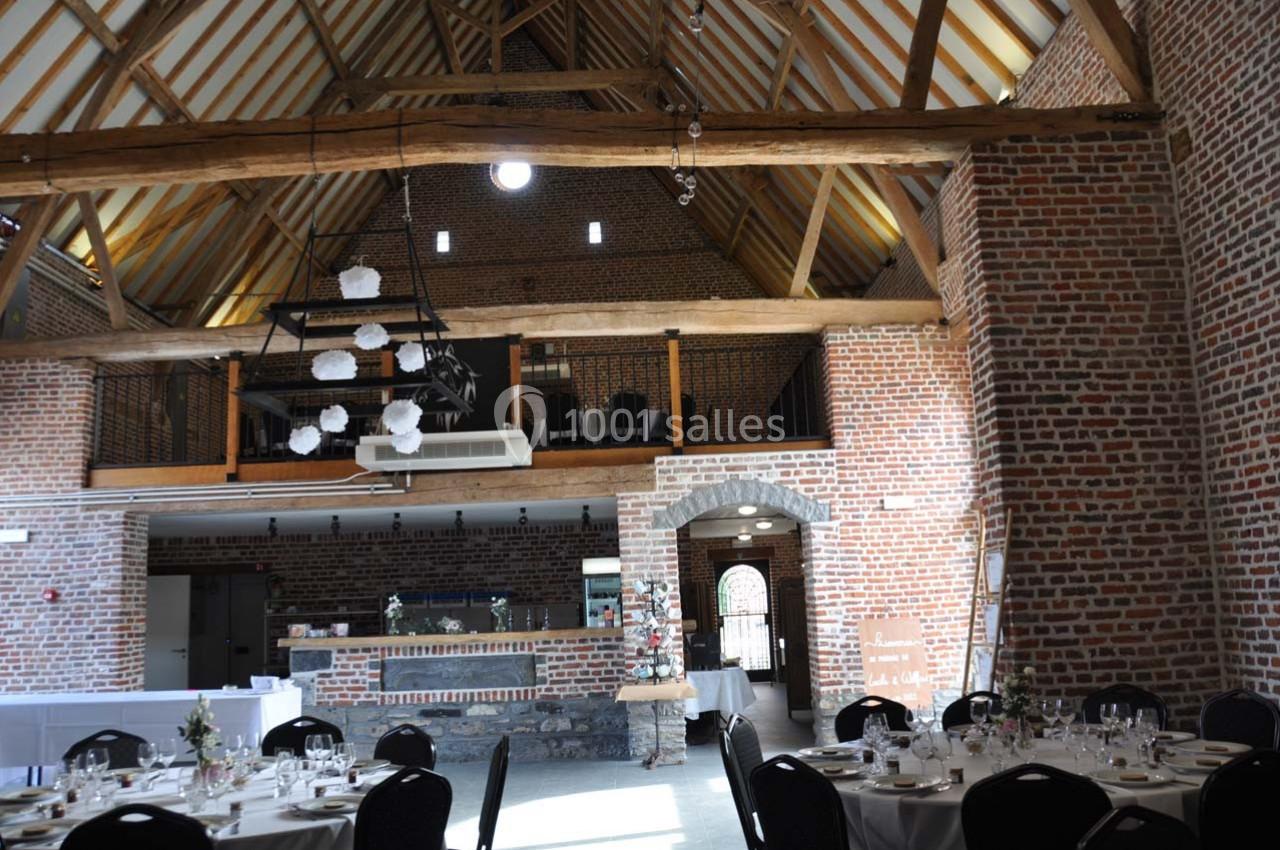 Salle de réception avec murs en briques, poutres apparentes et tables dressées pour un événement.