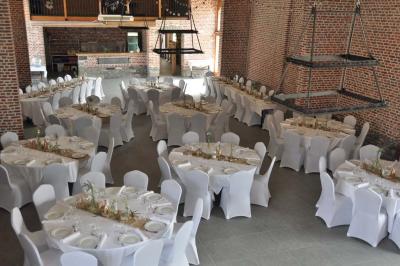 Salle de réception en briques avec tables rondes dressées, nappes blanches et décoration de mariage.
