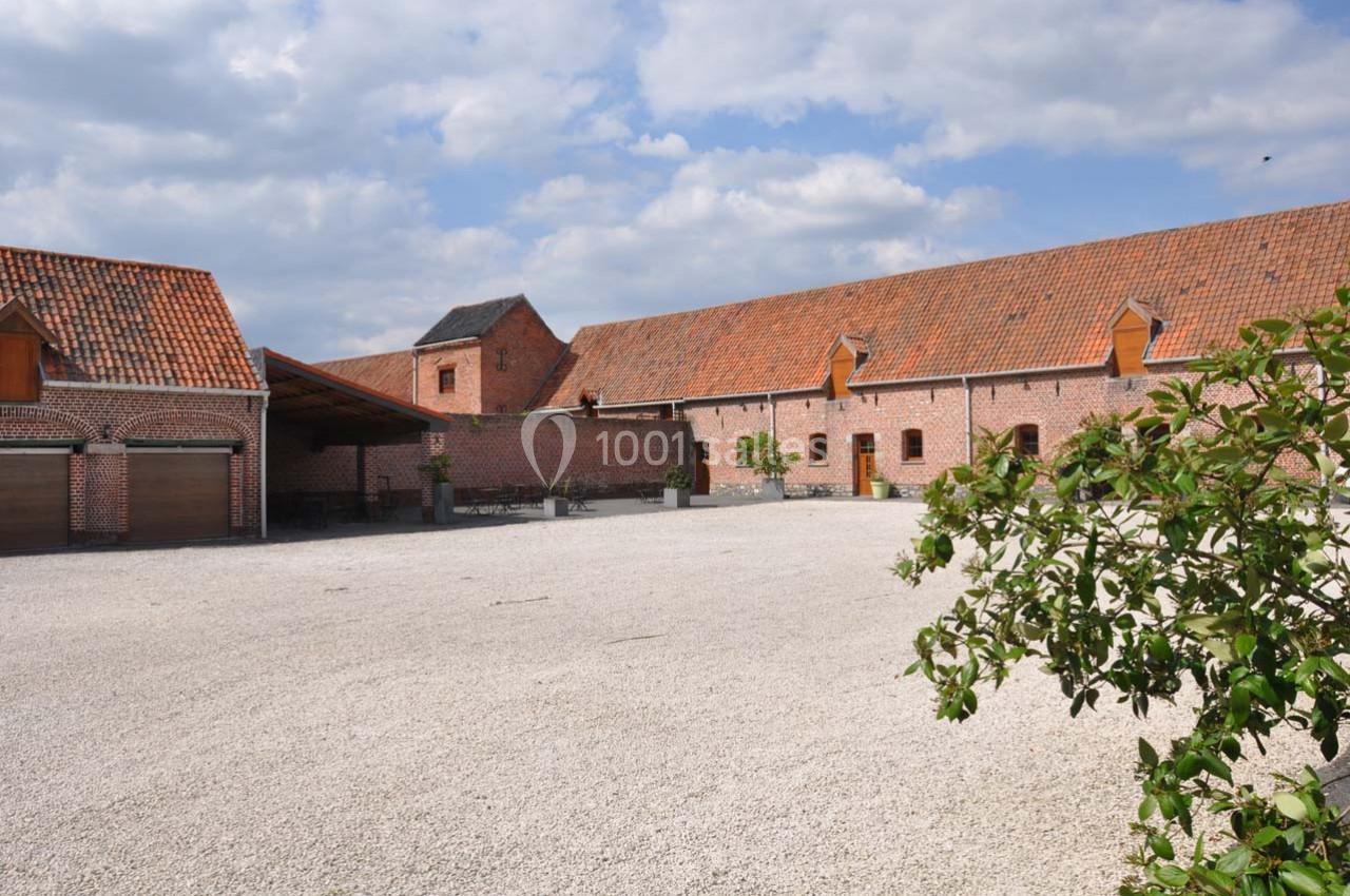 Cour pavée entourée de bâtiments en briques rouges avec toits en tuiles, sous un ciel partiellement nuageux.