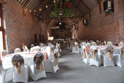 Salle de réception en briques avec tables rondes dressées, nappes blanches et décoration de mariage.
