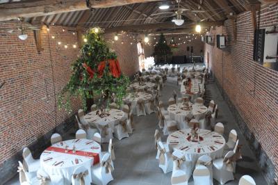 Salle de réception en briques avec tables rondes dressées, nappes blanches et décoration de mariage.