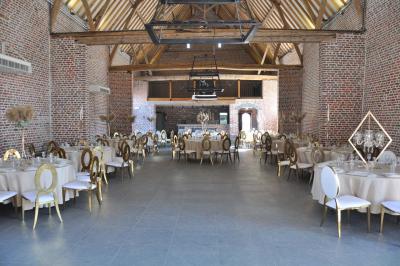 Salle de réception en briques avec tables rondes dressées, nappes blanches et décoration de mariage.
