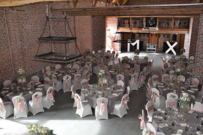 Salle de réception en briques avec tables rondes dressées, nappes blanches et décoration de mariage.