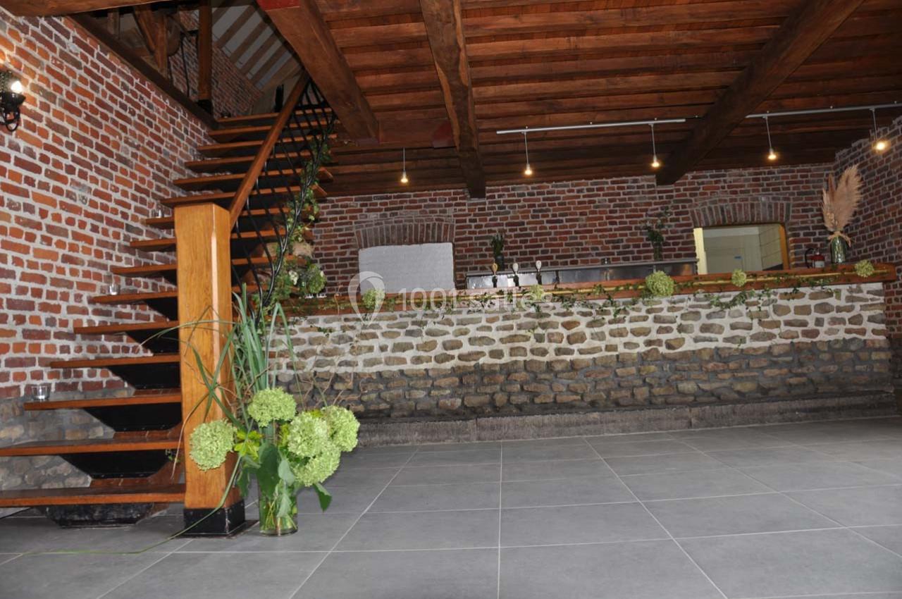 Intérieur d'une salle en briques et pierres apparentes avec escalier en bois et décoration végétale.