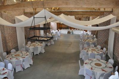 Salle de réception en briques avec tables rondes dressées, nappes blanches et décoration de mariage.