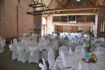 Salle de réception en briques avec tables rondes dressées, nappes blanches et décoration de mariage.