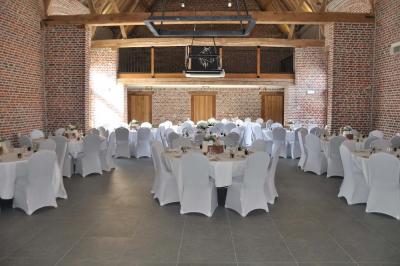 Salle de réception en briques avec tables rondes dressées, nappes blanches et décoration de mariage.