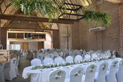 Salle de réception en briques avec tables rondes dressées, nappes blanches et décoration de mariage.