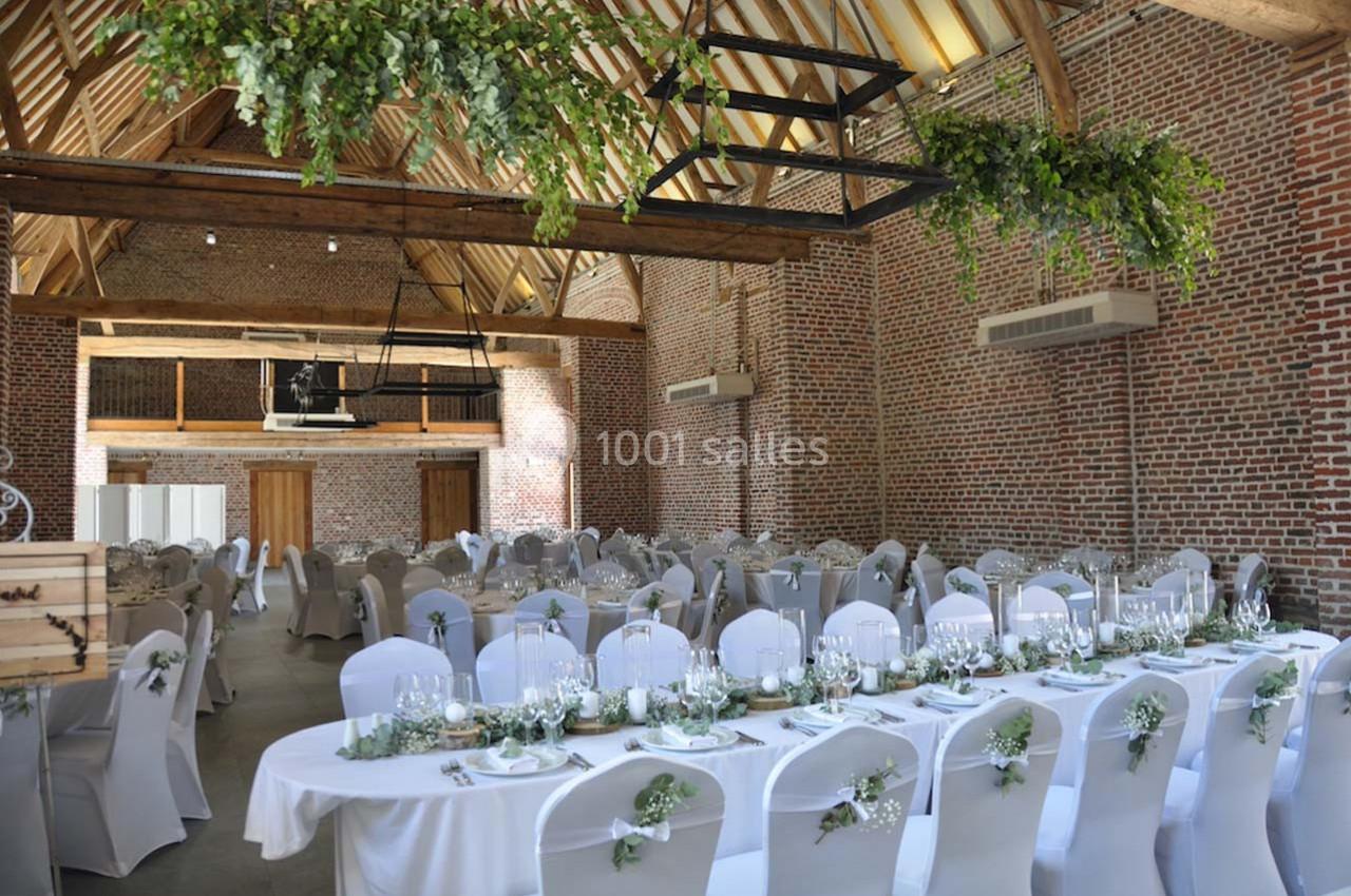 Salle de réception avec murs en briques, tables décorées de nappes blanches et feuillage suspendu au plafond.
