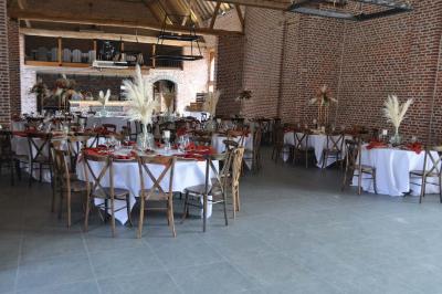Salle de réception en briques avec tables rondes dressées, nappes blanches et décoration de mariage.