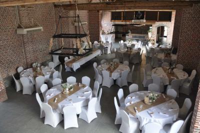 Salle de réception en briques avec tables rondes dressées, nappes blanches et décoration de mariage.