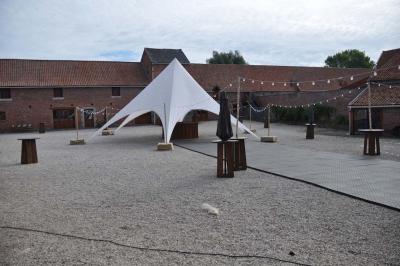Salle de réception en briques avec tables rondes dressées, nappes blanches et décoration de mariage.