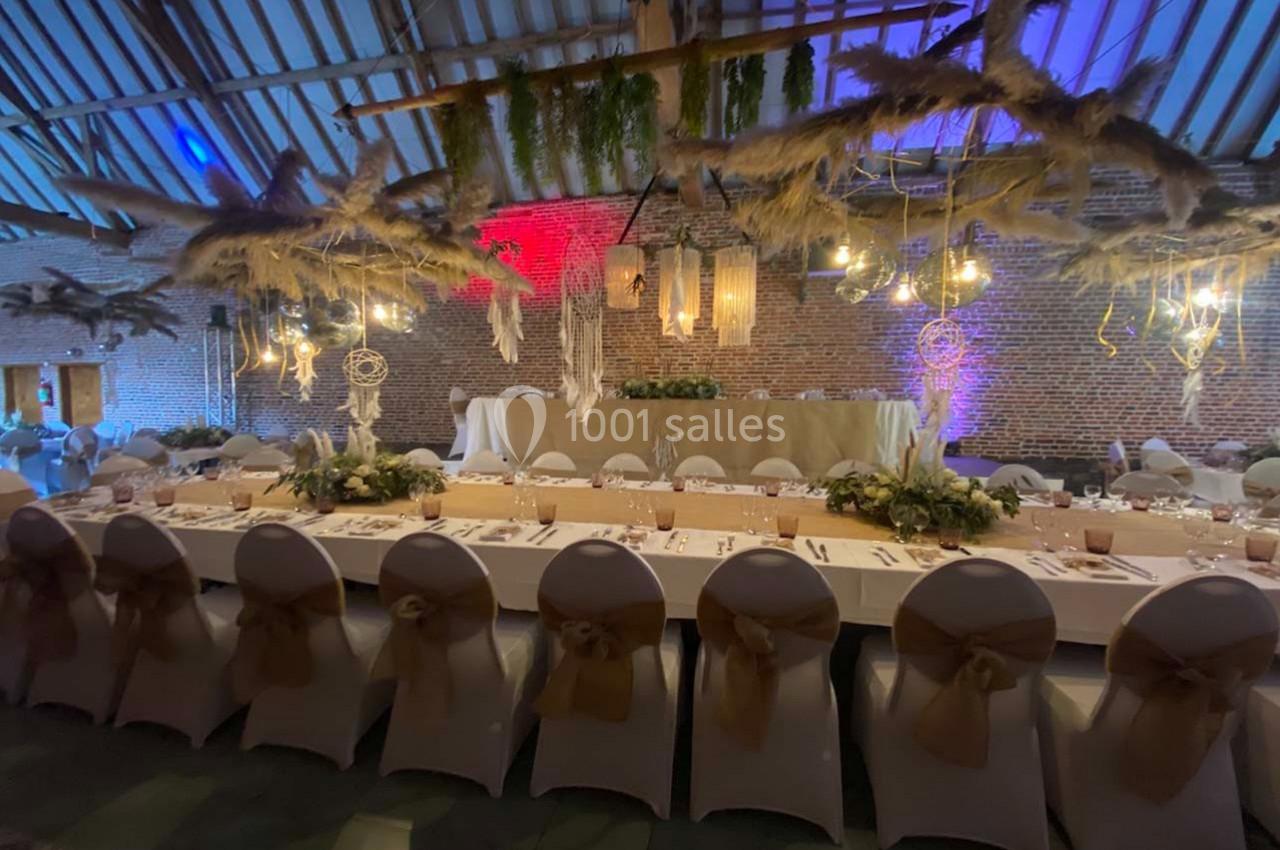 Salle de réception décorée avec des tables dressées, des chaises blanches et des suspensions végétales et lumineuses.
