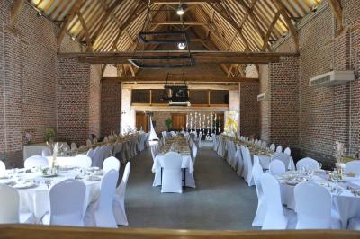 Salle de réception en briques avec tables rondes dressées, nappes blanches et décoration de mariage.
