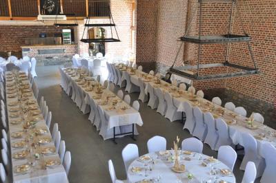 Salle de réception en briques avec tables rondes dressées, nappes blanches et décoration de mariage.