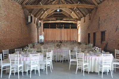 Salle de réception en briques avec tables rondes dressées, nappes blanches et décoration de mariage.