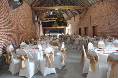 Salle de réception en briques avec tables rondes dressées, nappes blanches et décoration de mariage.