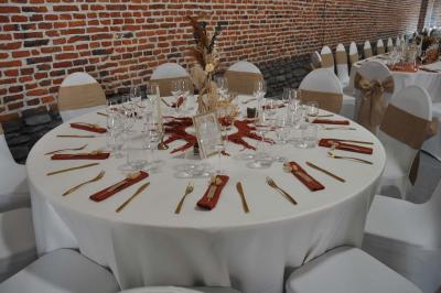 Salle de réception en briques avec tables rondes dressées, nappes blanches et décoration de mariage.