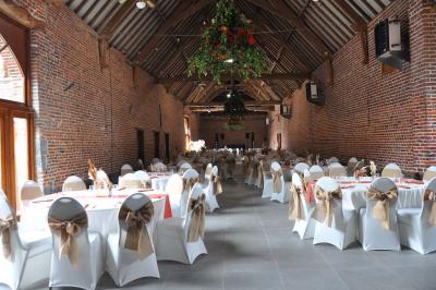 Salle de réception en briques avec tables rondes dressées, nappes blanches et décoration de mariage.