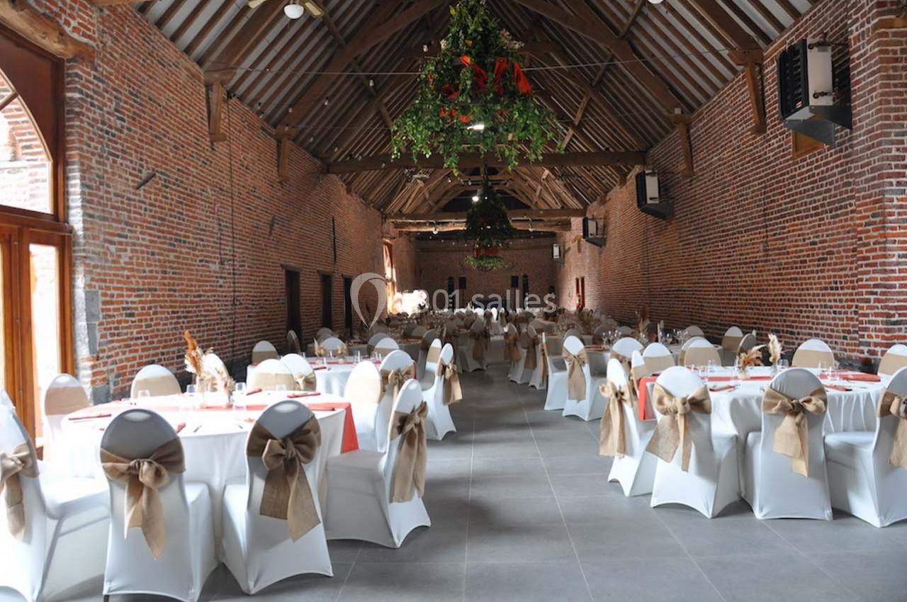 Salle de réception en briques avec des tables rondes dressées, chaises décorées de nœuds en toile de jute et plafond en…