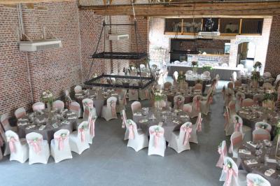 Salle de réception en briques avec tables rondes dressées, nappes blanches et décoration de mariage.