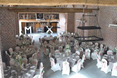 Salle de réception en briques avec tables rondes dressées, nappes blanches et décoration de mariage.