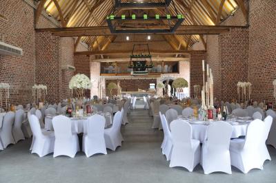 Salle de réception en briques avec tables rondes dressées, nappes blanches et décoration de mariage.