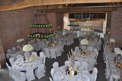 Salle de réception en briques avec tables rondes dressées, nappes blanches et décoration de mariage.