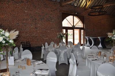 Salle de réception en briques avec tables rondes dressées, nappes blanches et décoration de mariage.