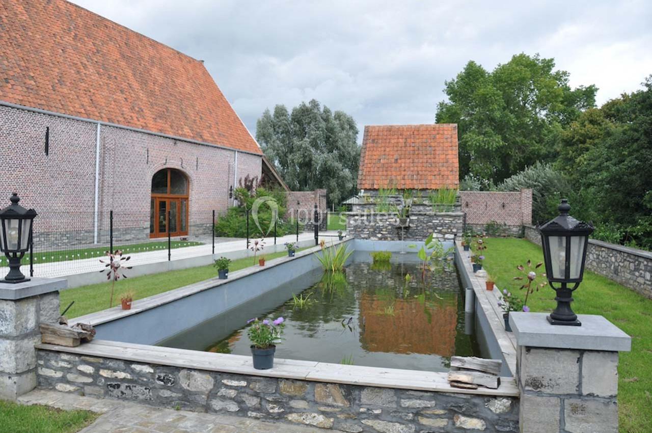 Étang rectangulaire entouré de pelouse, avec des lampadaires et des bâtiments en briques aux toits rouges en arrière-plan.