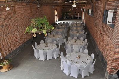 Salle de réception en briques avec tables rondes dressées, nappes blanches et décoration de mariage.