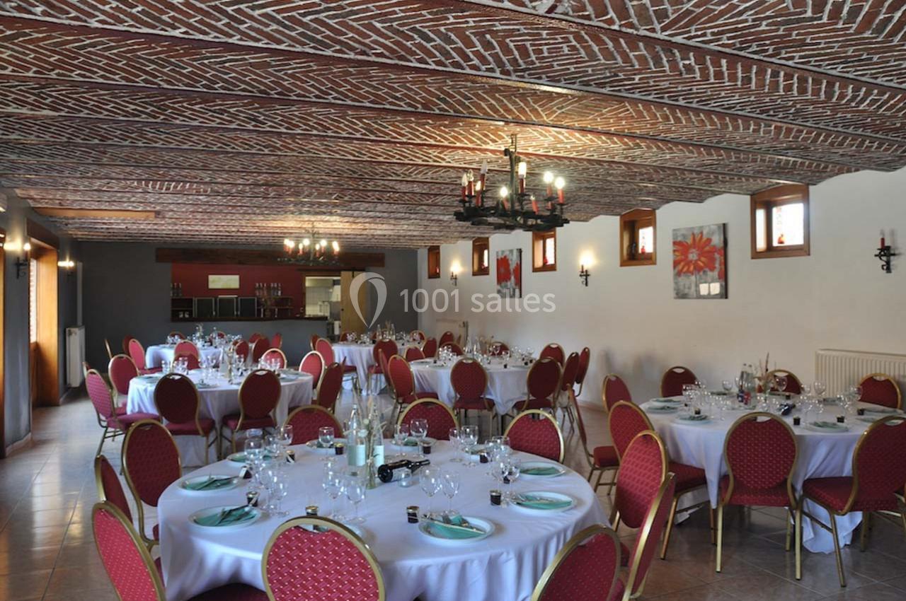Salle de réception avec tables rondes dressées, chaises rouges et plafond en briques apparentes.