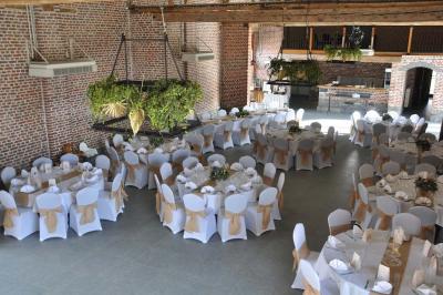 Salle de réception en briques avec tables rondes dressées, nappes blanches et décoration de mariage.