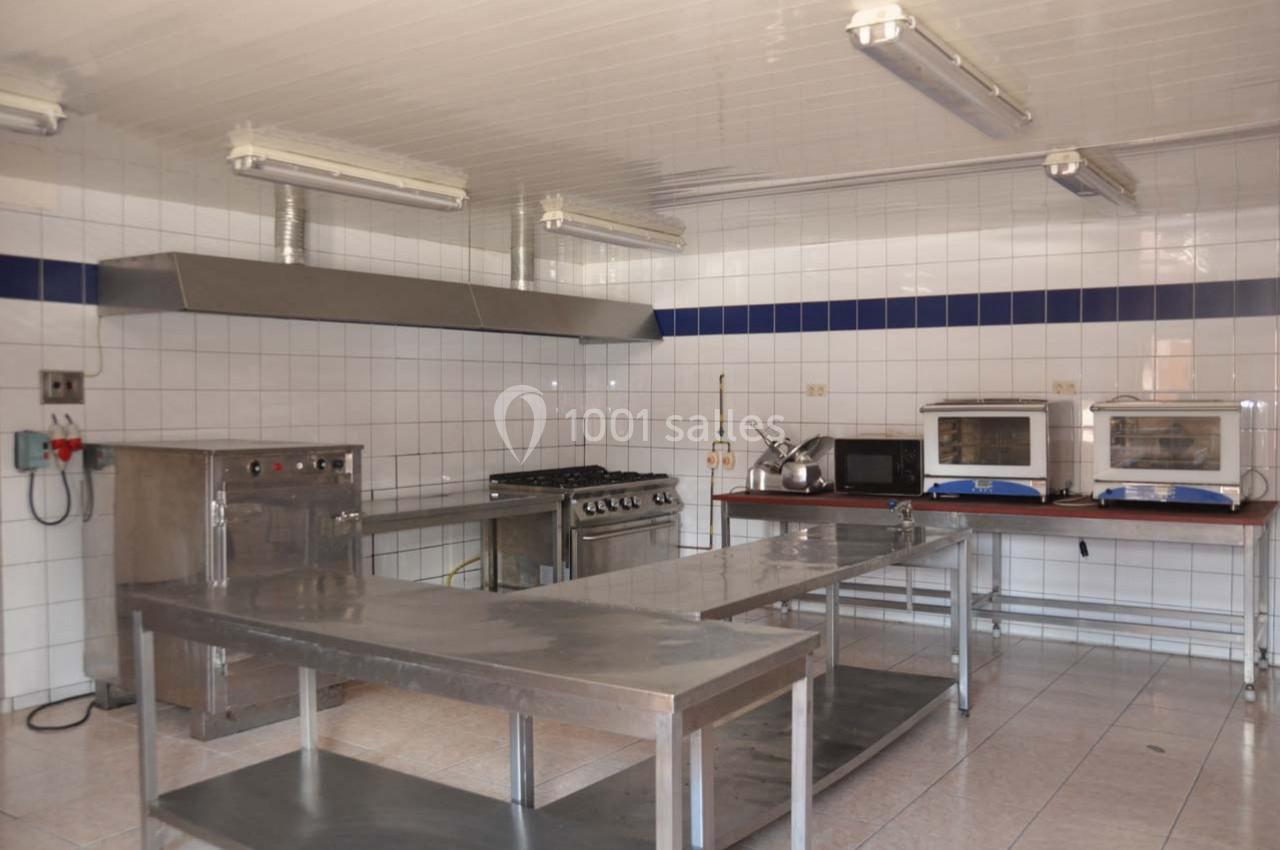 Cuisine professionnelle équipée avec plans de travail en inox, fours, plaques de cuisson et carrelage mural blanc.