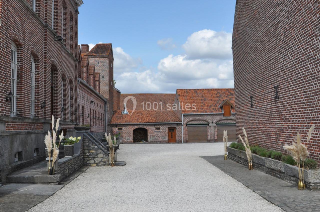 Cour pavée entourée de bâtiments en briques rouges avec des toits en tuiles et des décorations végétales.