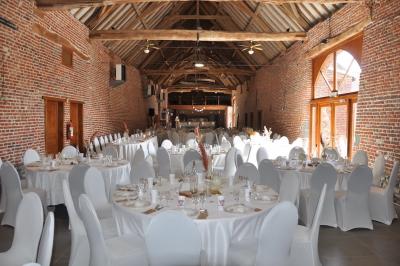 Salle de réception en briques avec tables rondes dressées, nappes blanches et décoration de mariage.