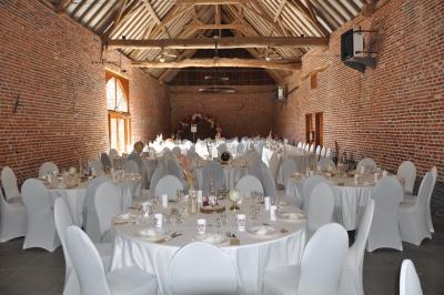 Salle de réception en briques avec tables rondes dressées, nappes blanches et décoration de mariage.
