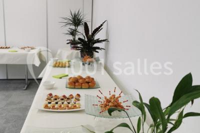 Table garnie de petits fours, desserts et plantes décoratives dans une salle lumineuse avec murs blancs.