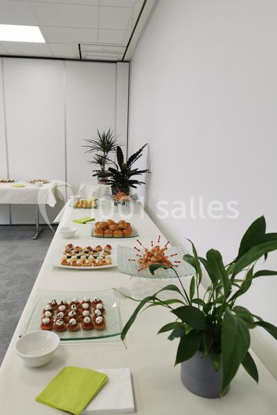 Table garnie de petits fours, desserts et plantes décoratives dans une salle lumineuse avec murs blancs.